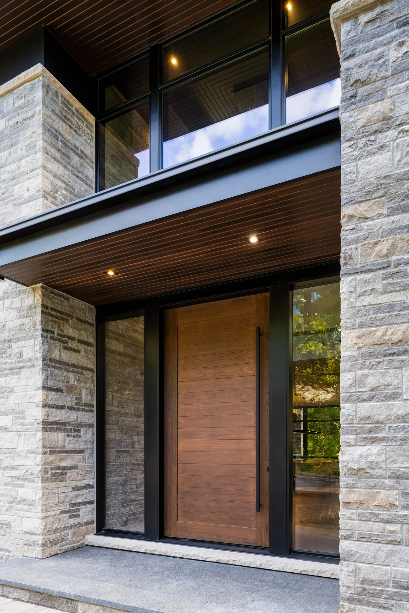 Tall woodgrain front door with sidelights and light stone wall